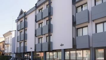 Un edificio moderno de varios pisos con balcones, ventanas amplias y un automóvil estacionado.