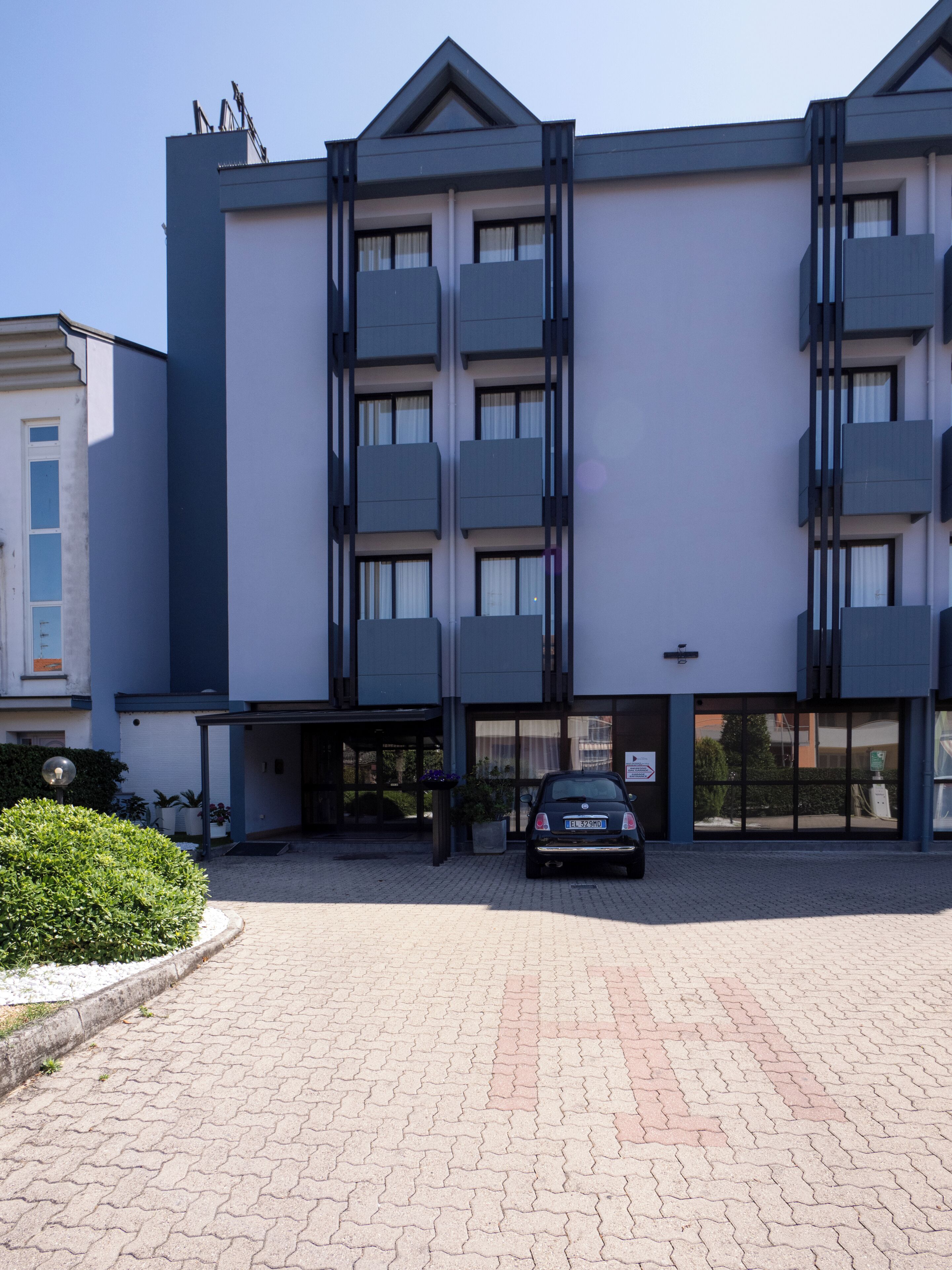 A modern building with a symmetrical facade, multiple balconies, and a paved entrance area.