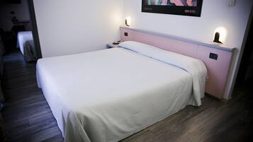 Un lit bien fait, recouvert d’une couvre-lit blanche, une table de chevet avec une lampe et une œuvre d’art accrochée au mur.