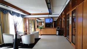 A modern hotel lobby with a reception desk, seating area, and a television screen. - Hotel Ilga (Collecchio)