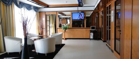 A modern hotel lobby with a reception desk, seating area, and a television screen.