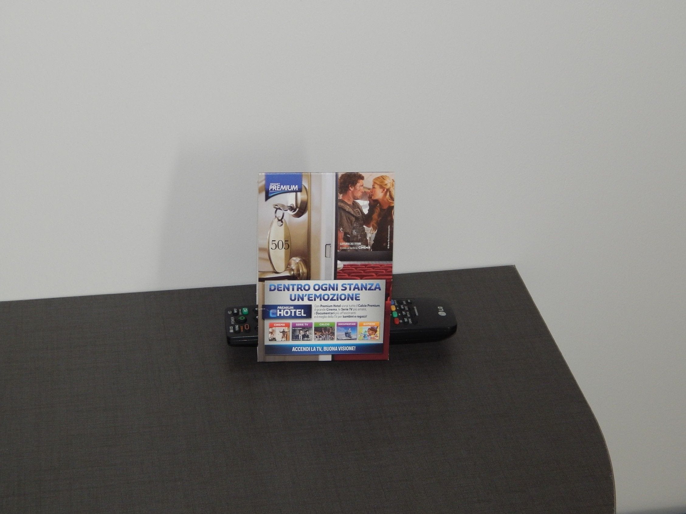 Exhibición promocional de un hotel que incluye un control remoto, un televisor y un letrero que indica servicios como cine, televisión y desayuno.