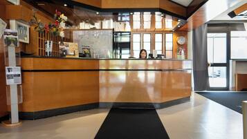 Uma área de recepção de hotel com carpete preto, balcão de madeira e um relógio na parede.