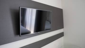 Une chambre moderne avec un téléviseur à écran plat fixé sur un mur sombre, une table en verre et une chaise blanche.