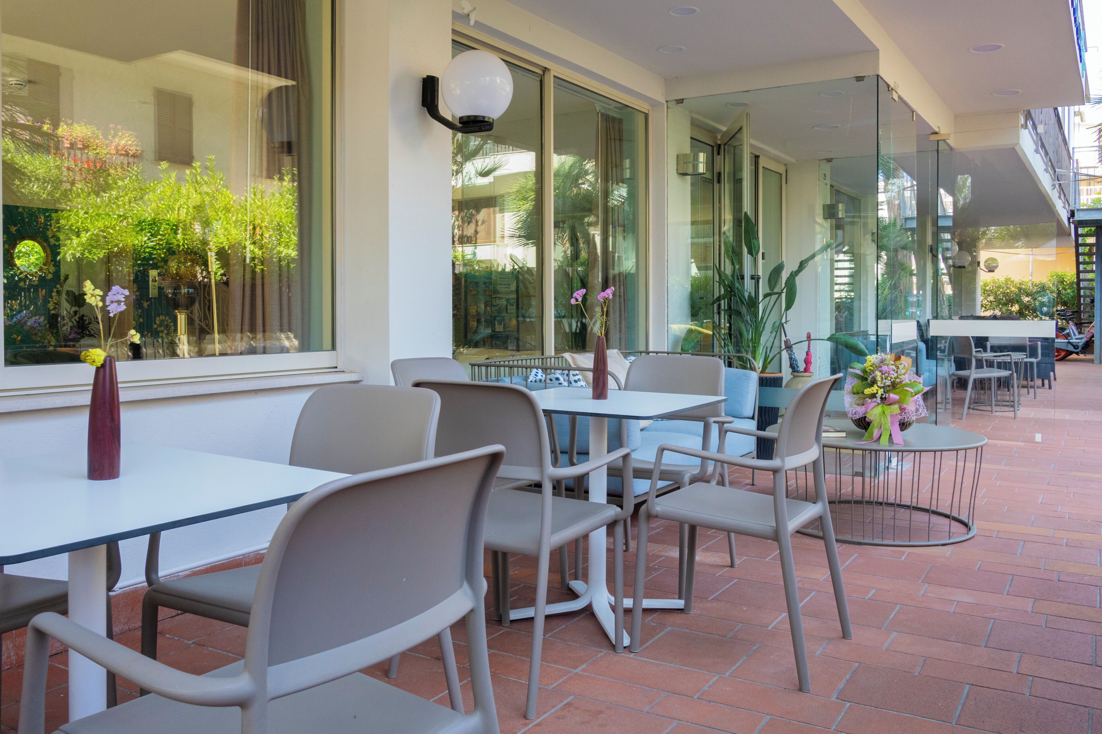 Un área de estar al aire libre con mesas y sillas, ventanas amplias con vistas a la vegetación y un diseño moderno.