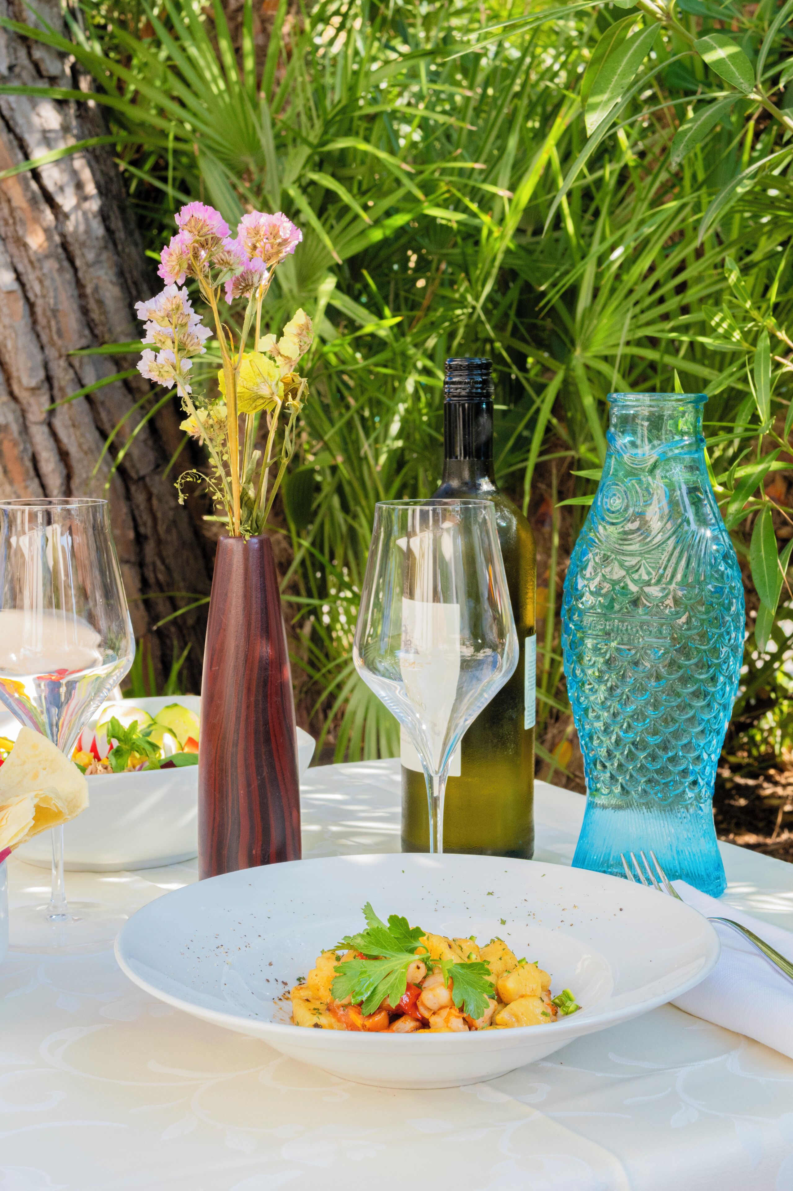 A table with a white plate of food, two wine glasses, and three decorative vases.