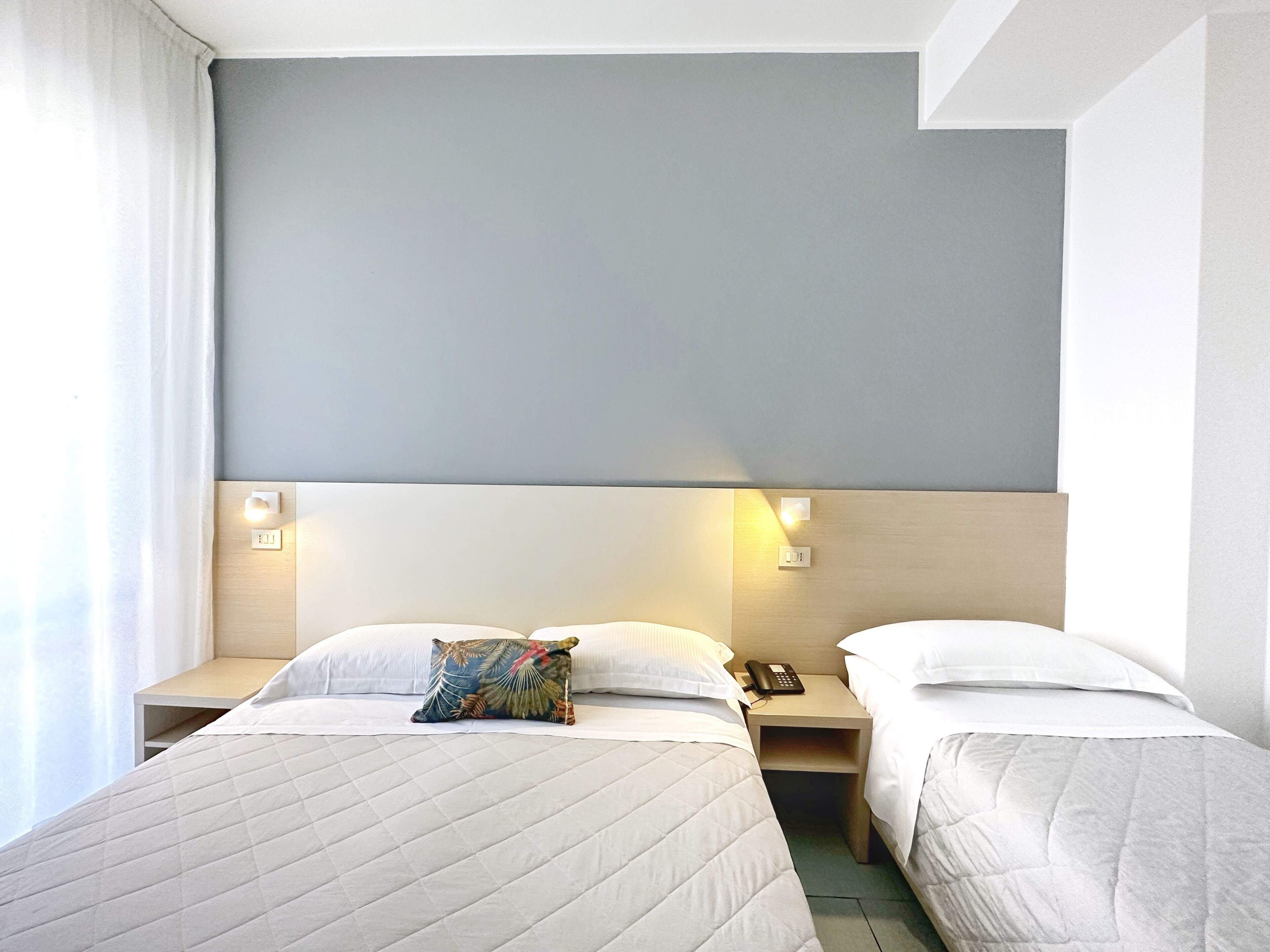 A hotel room with two beds, each with a pillow and a bedside table with a phone.