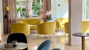 A modern dining area with yellow and blue chairs, marble tables, and a view of greenery outside.