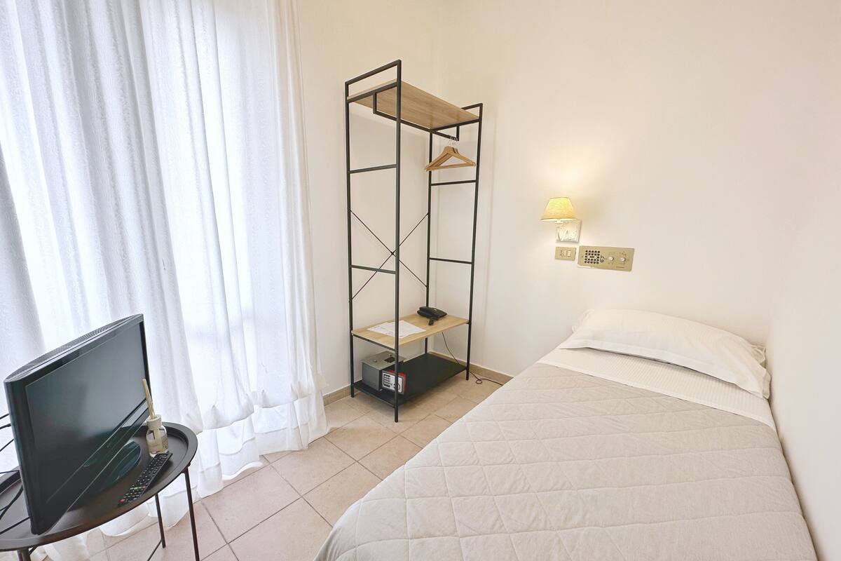 A hotel room with a bed, a TV on a small table, a wardrobe, and a lamp.