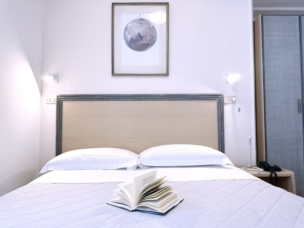 A neatly made bed with white linens and pillows, a framed picture on the wall, and a bedside table with a phone.