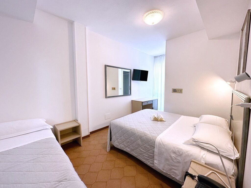 Habitación de hotel con dos camas, un televisor montado en la pared, una mesita de noche y una lámpara.