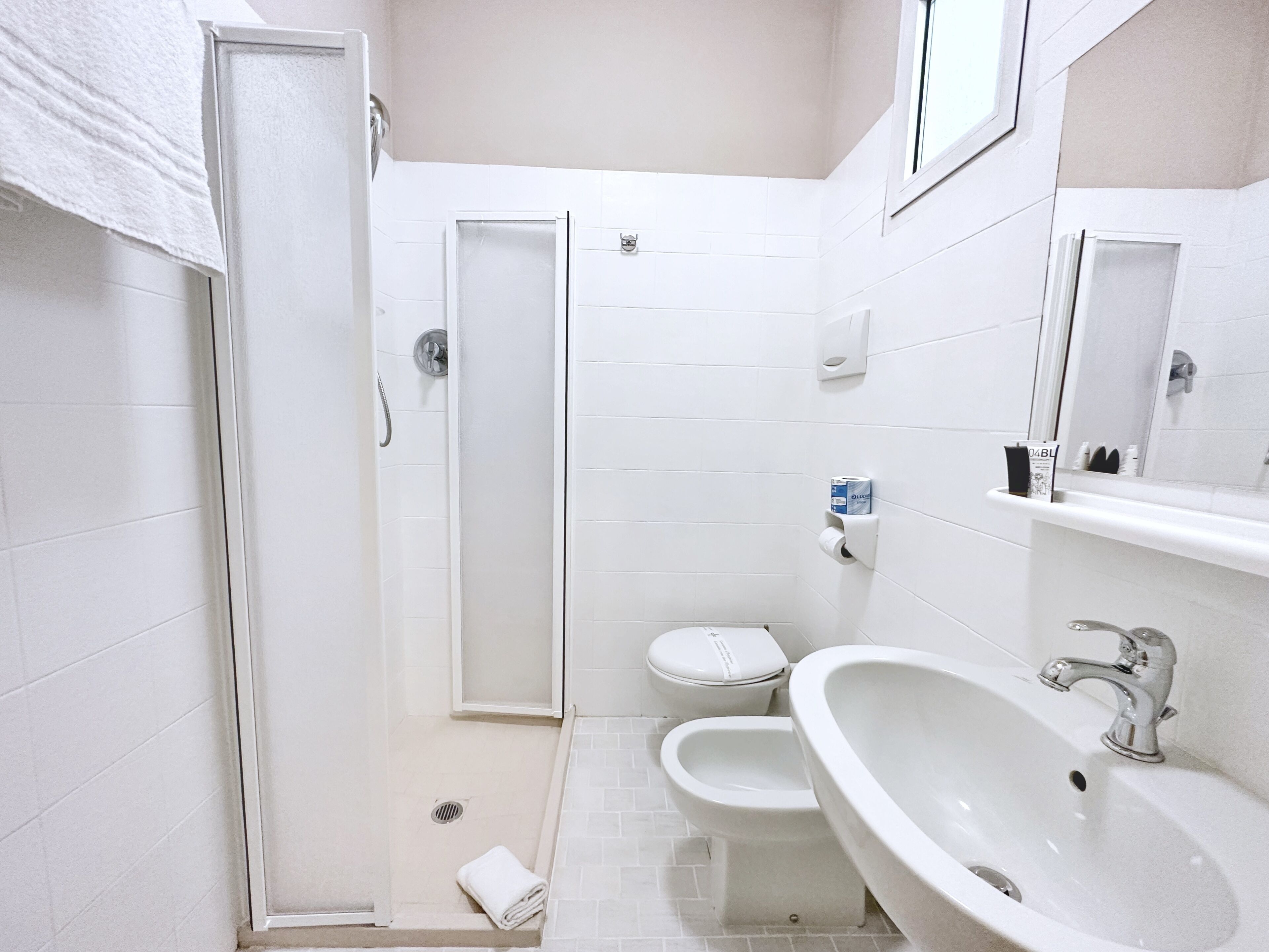 A bathroom with a shower, toilet, bidet, and sink.
