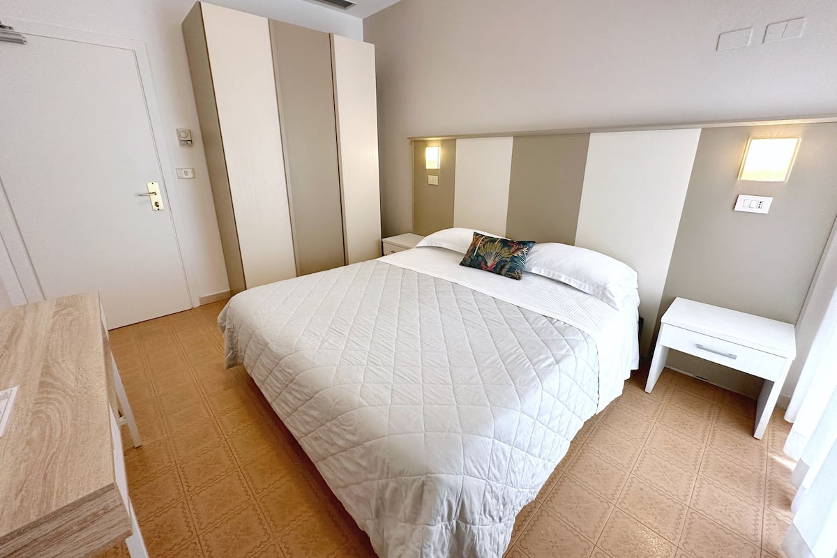 A bedroom with a bed, a bedside table, a wardrobe, and a desk.