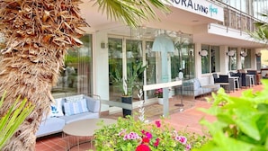 A hotel with a modern design, featuring a glass facade, outdoor seating area, and a palm tree.