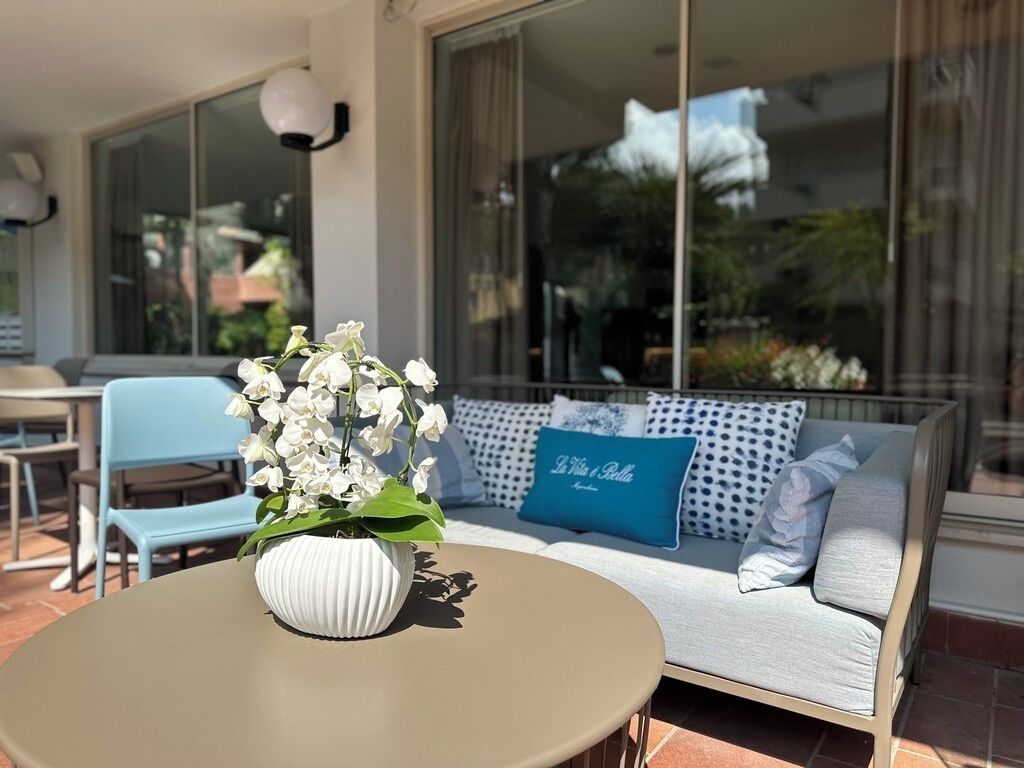 Een moderne buiten zithoek met een ronde tafel, een bank met gestreepte kussens en een vaas witte bloemen.