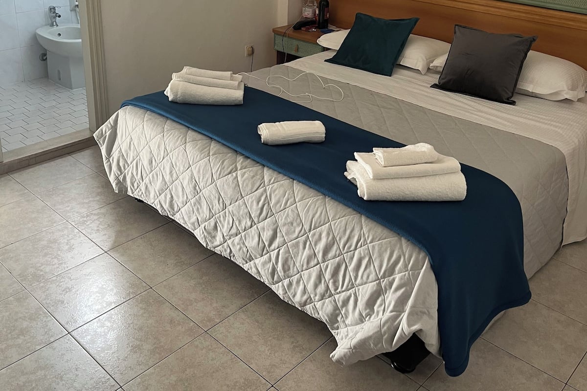 A hotel room with a bed, a nightstand, a bathroom visible through an open door, and a tiled floor.