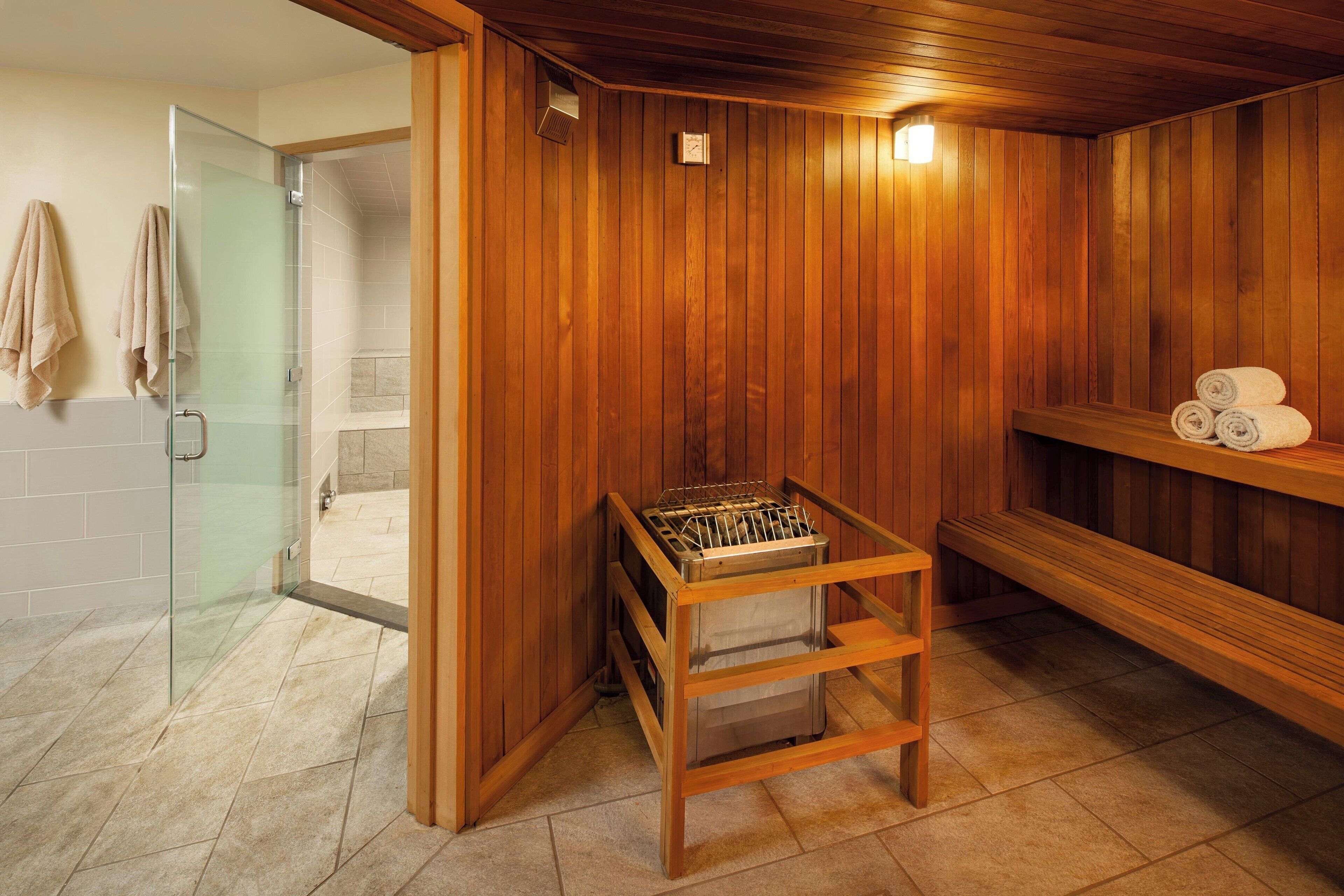 Un sauna aux murs en bois, une porte en verre donnant sur un espace douche et une étagère avec des serviettes.
