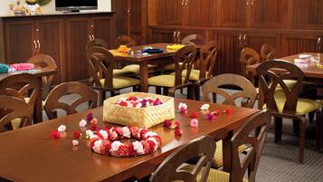 A dining area with wooden tables and chairs, a basket of flowers, and a television on the wall.