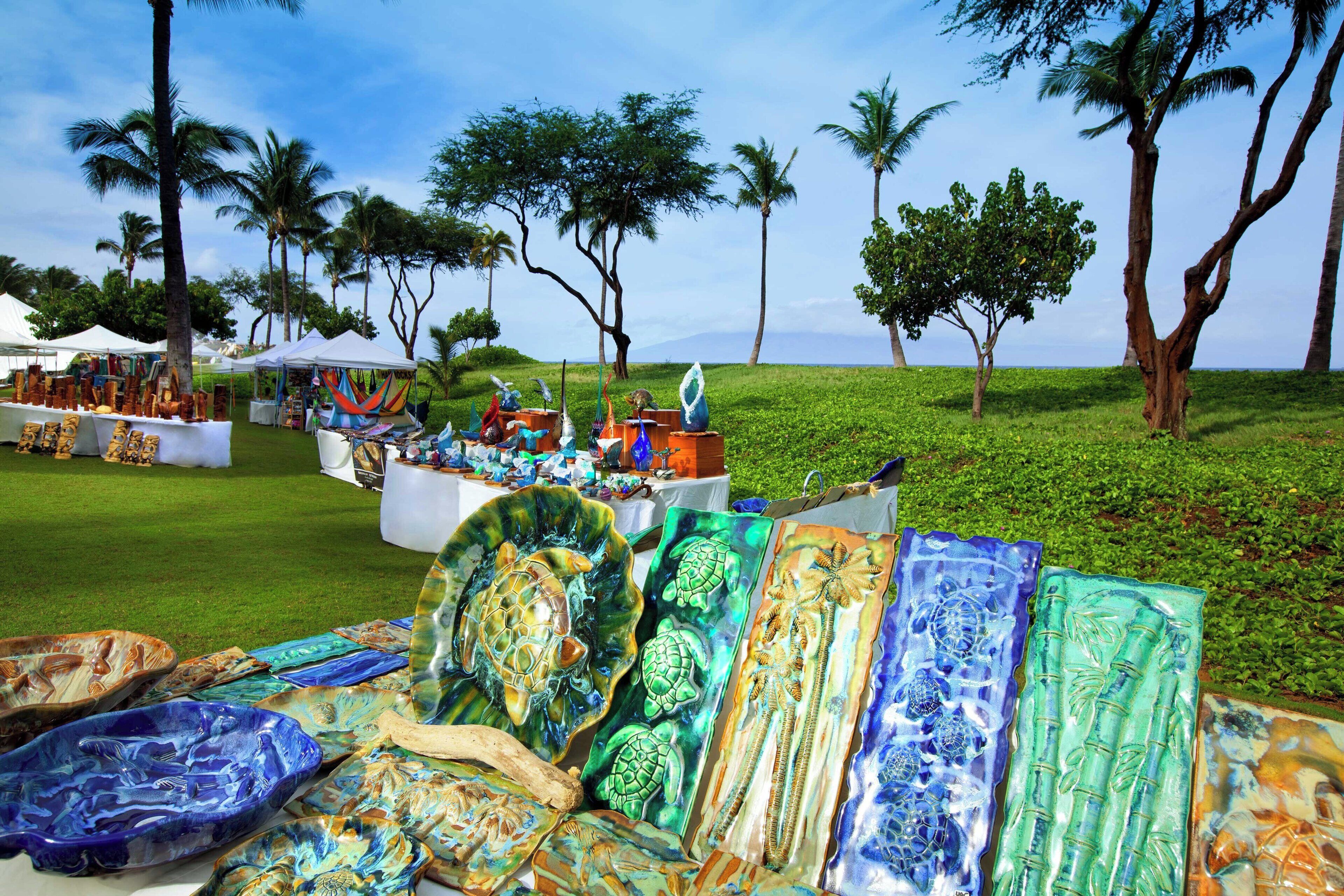 A beachside market with various colorful glass art pieces displayed on tables.