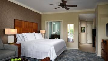 A hotel room with a large bed, a desk, a chair, a TV, and a ceiling fan.