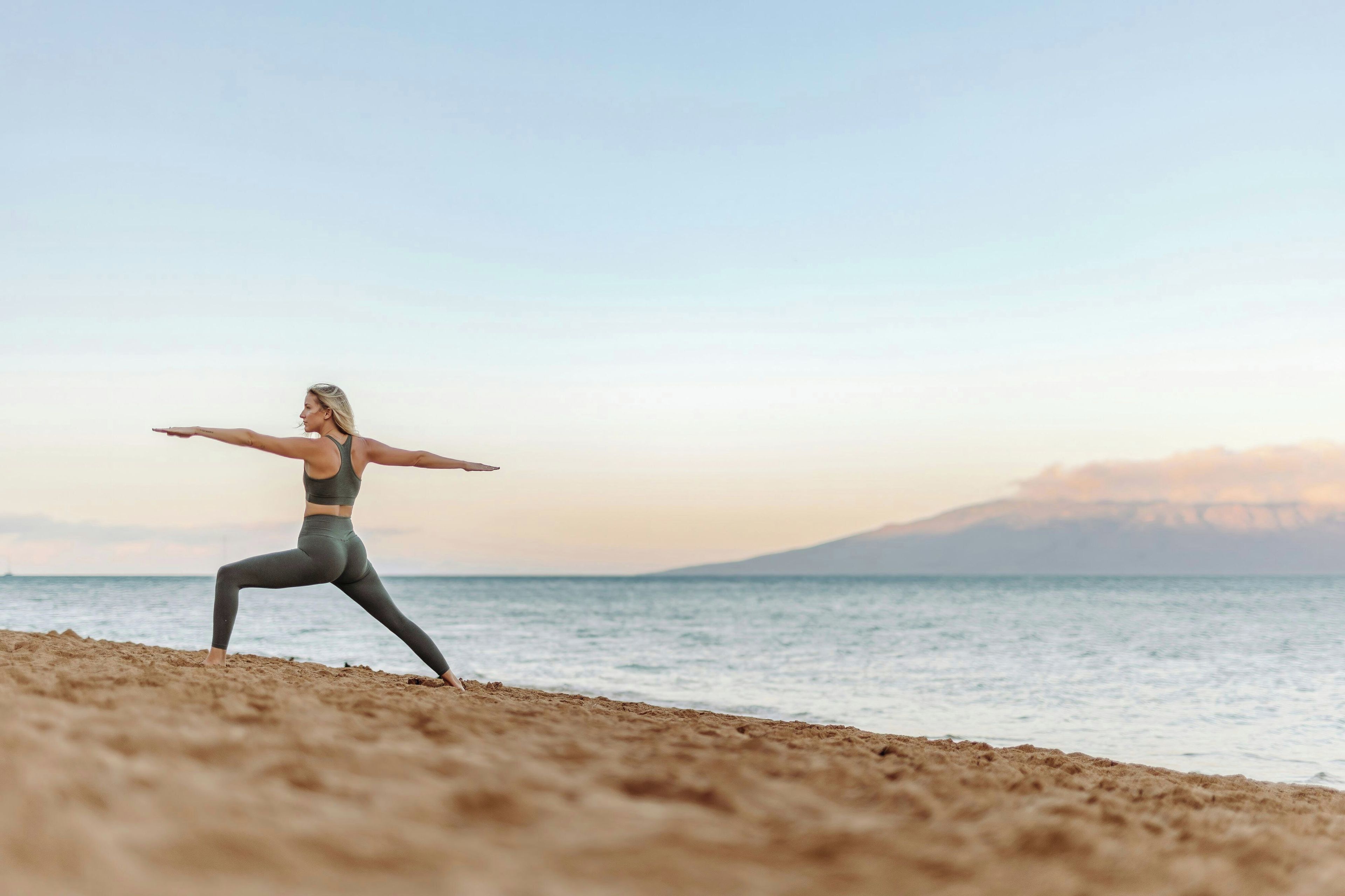 A person performing a yoga pose on a beach with a mountain in the background.
