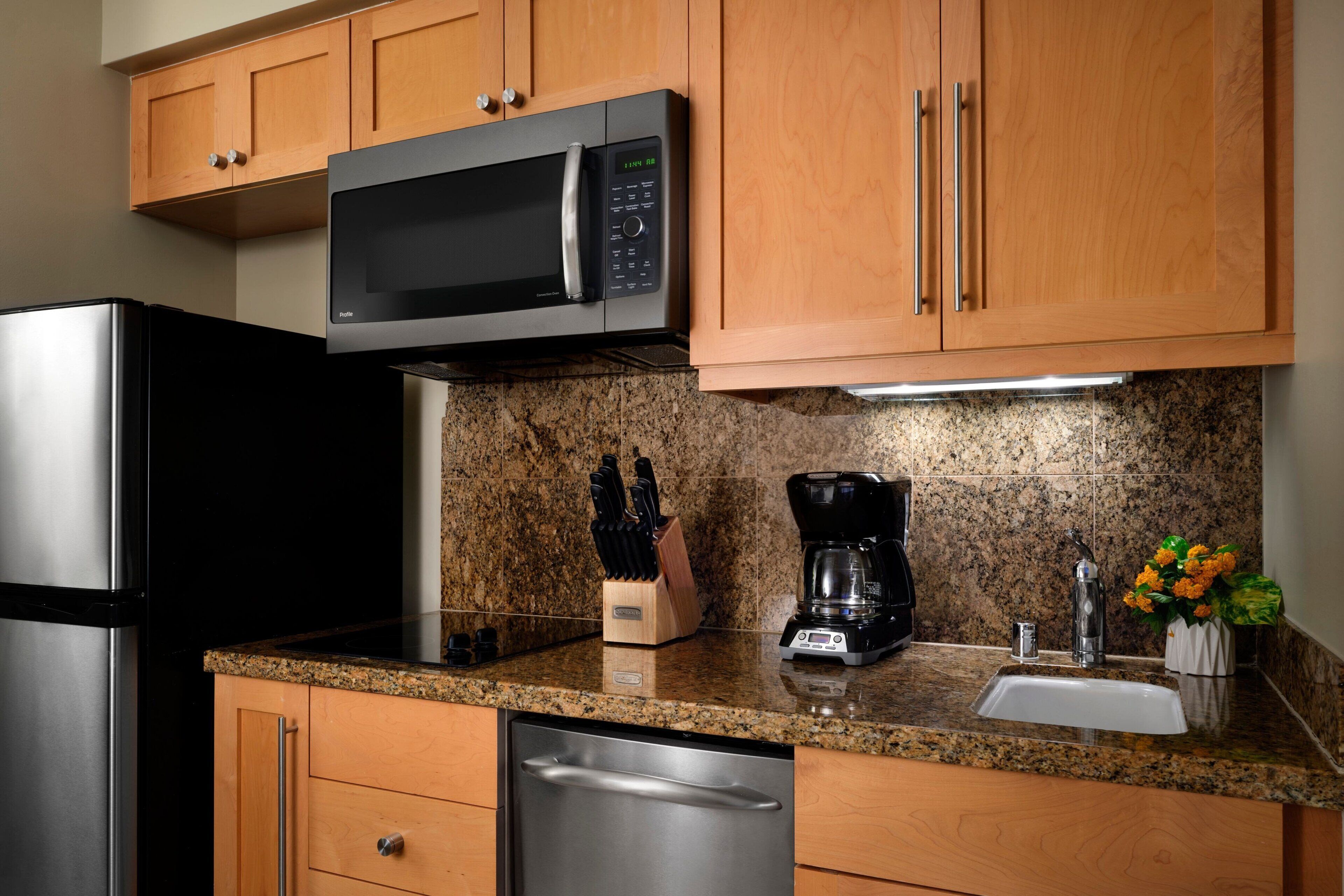 A kitchen with wooden cabinets, a stainless steel refrigerator, a microwave, a coffee maker, and a dishwasher.