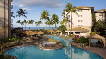 A resort pool area with multiple pools, lounge chairs, umbrellas, and palm trees.