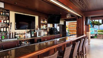 Un espace bar avec un long comptoir, de nombreuses bouteilles d’alcool, un téléviseur fixé au mur et une vue sur l’extérieur.