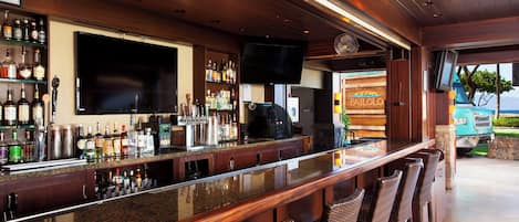A bar area with a long counter, multiple liquor bottles, a TV mounted on the wall, and a view of the outside.