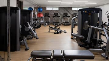 Uma academia com diversos equipamentos de exercícios, incluindo esteiras, aparelhos de musculação e um banco.