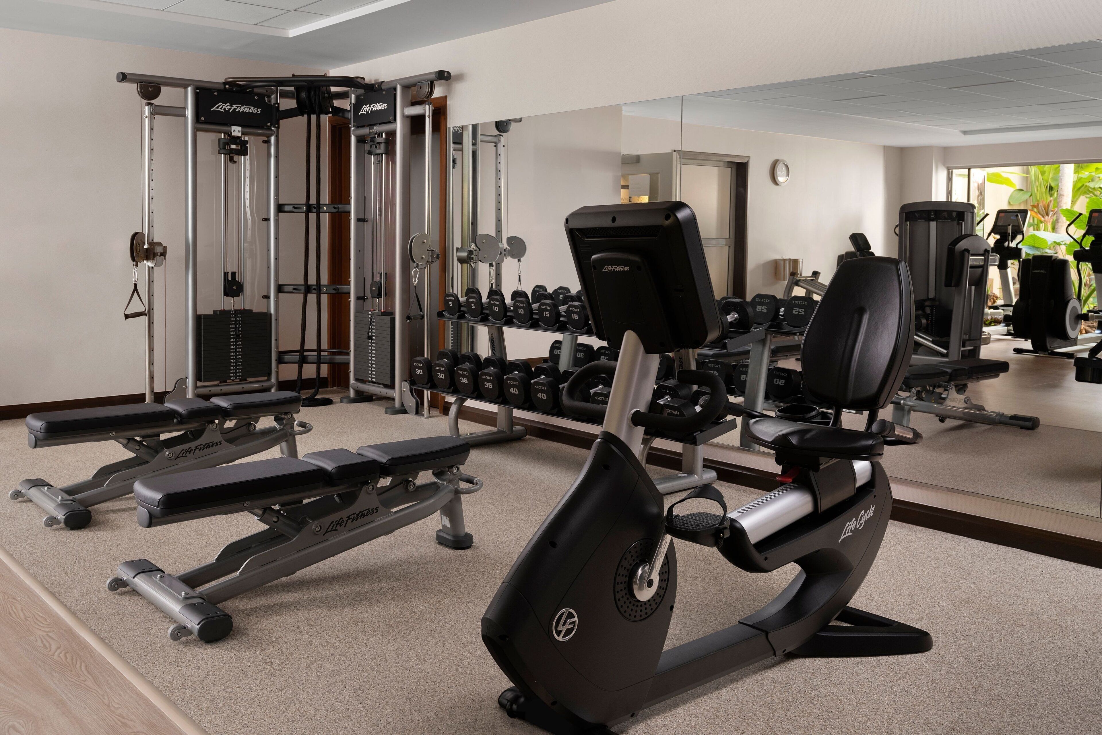 A gym with cardio machines, weightlifting equipment, and dumbbells.