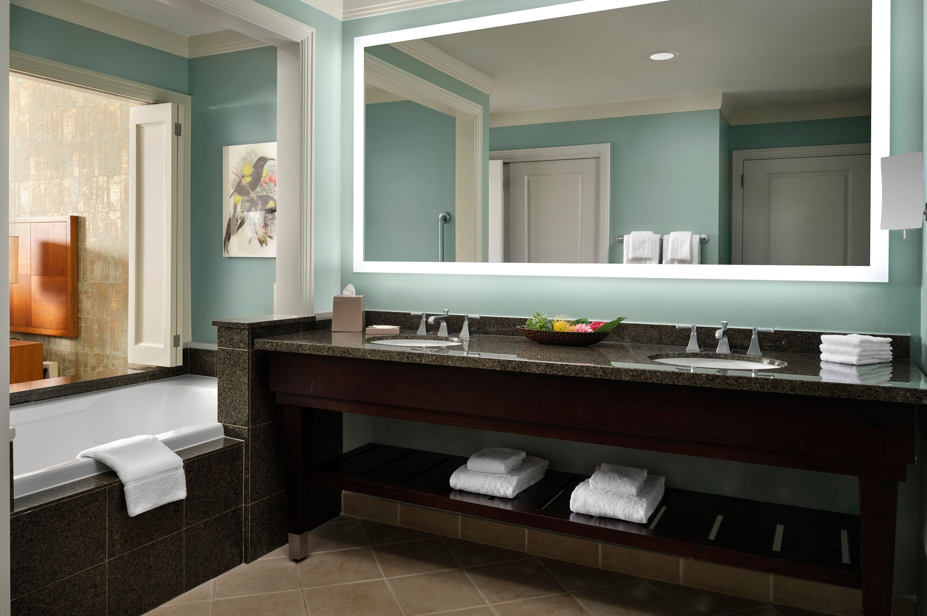 A bathroom with a bathtub, a large mirror, a vanity with a sink, and a shelf with towels.