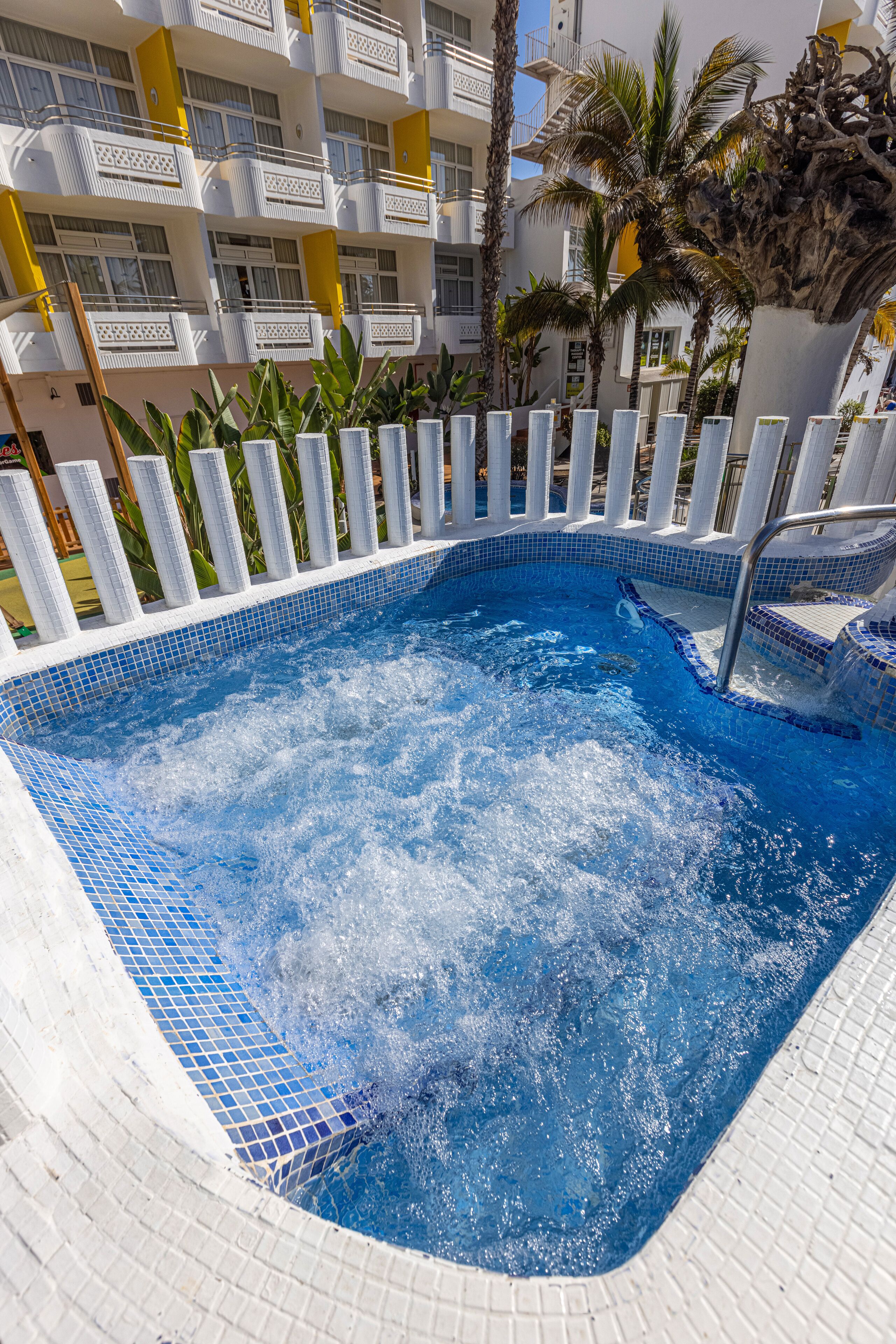 Una piscina amb vora enrajolada, envoltada per una tanca blanca i palmeres.