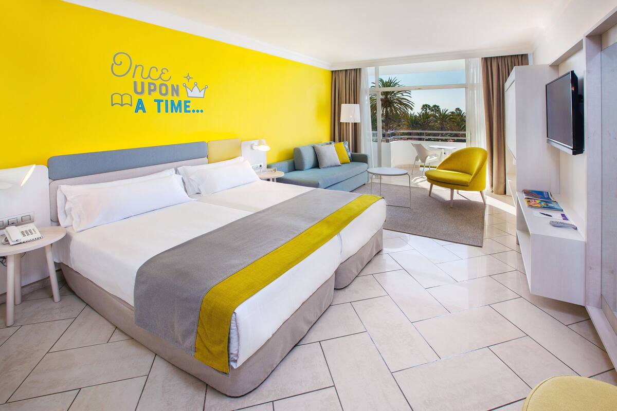 A hotel room with a large bed, a sofa, a chair, a desk, and a TV.