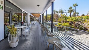 A covered outdoor seating area with tables and chairs, overlooking a landscaped garden with palm trees. - Abora Catarina by Lopesan Hotels - All Inclusive (San Bartolomé de Tirajana)