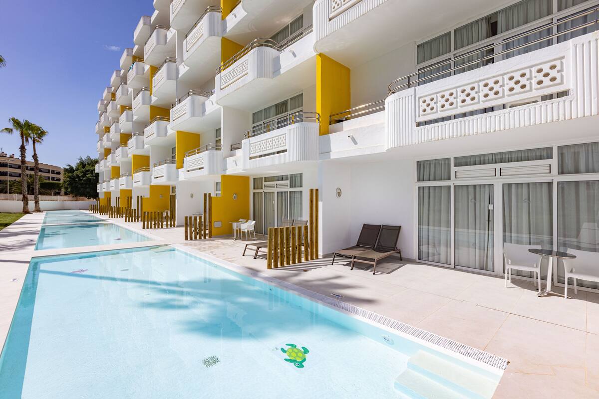 A hotel with multiple balconies, a swimming pool, and outdoor seating areas.
