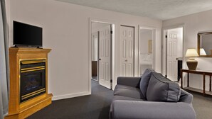 A living room with a fireplace, a gray sofa, and a television on a stand. - Traverse Bay Inn (Traverse City)