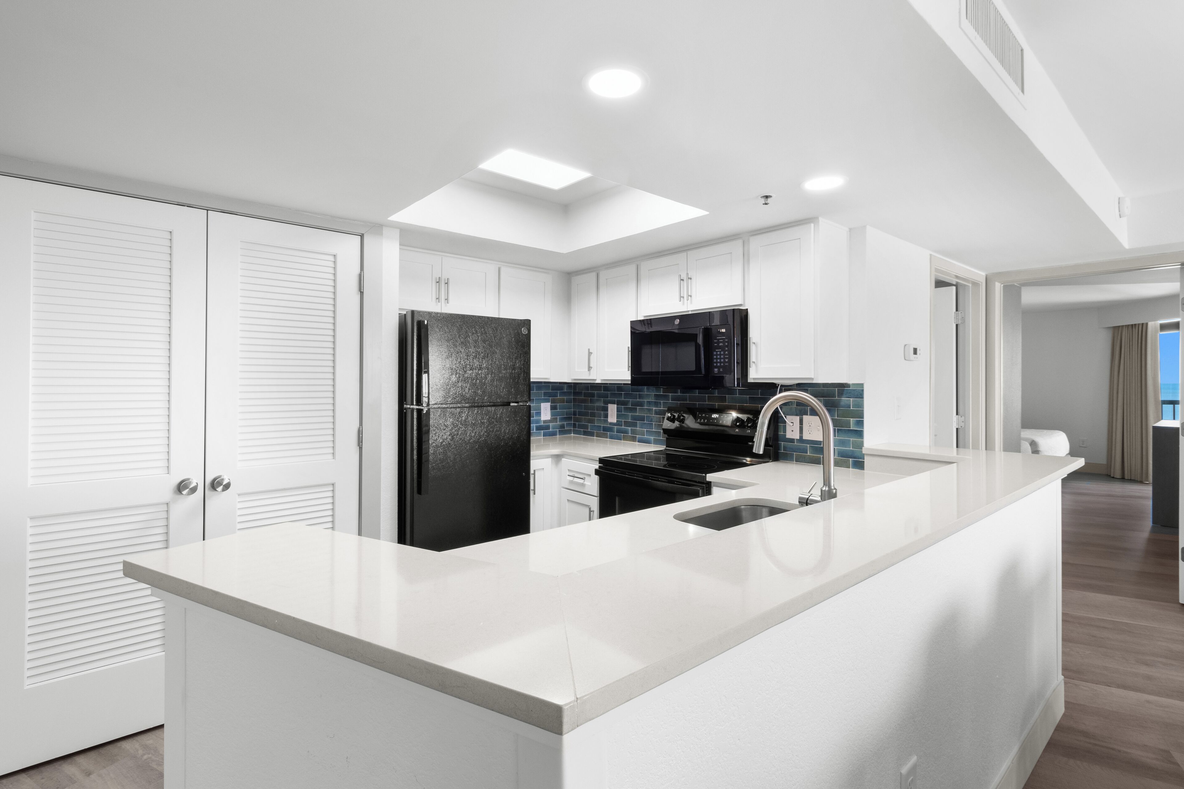A modern kitchen with white cabinetry, a black refrigerator, a microwave, and a large island with a sink.