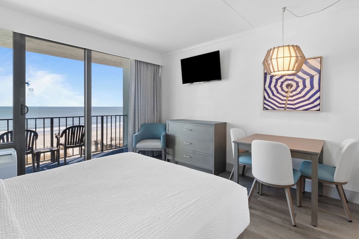 A hotel room with a bed, a desk with chairs, a TV, and a painting.