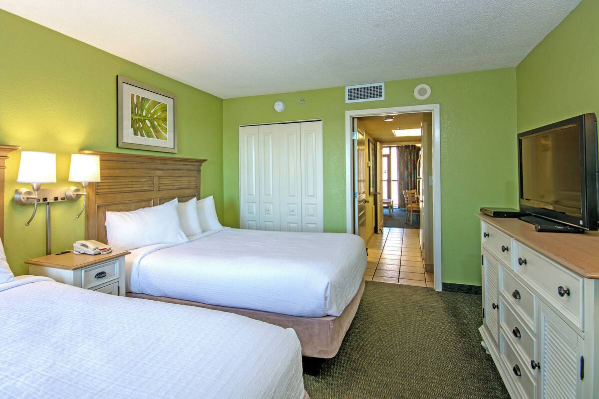 A hotel room with two beds, a TV, a dresser, and a door leading to a hallway.