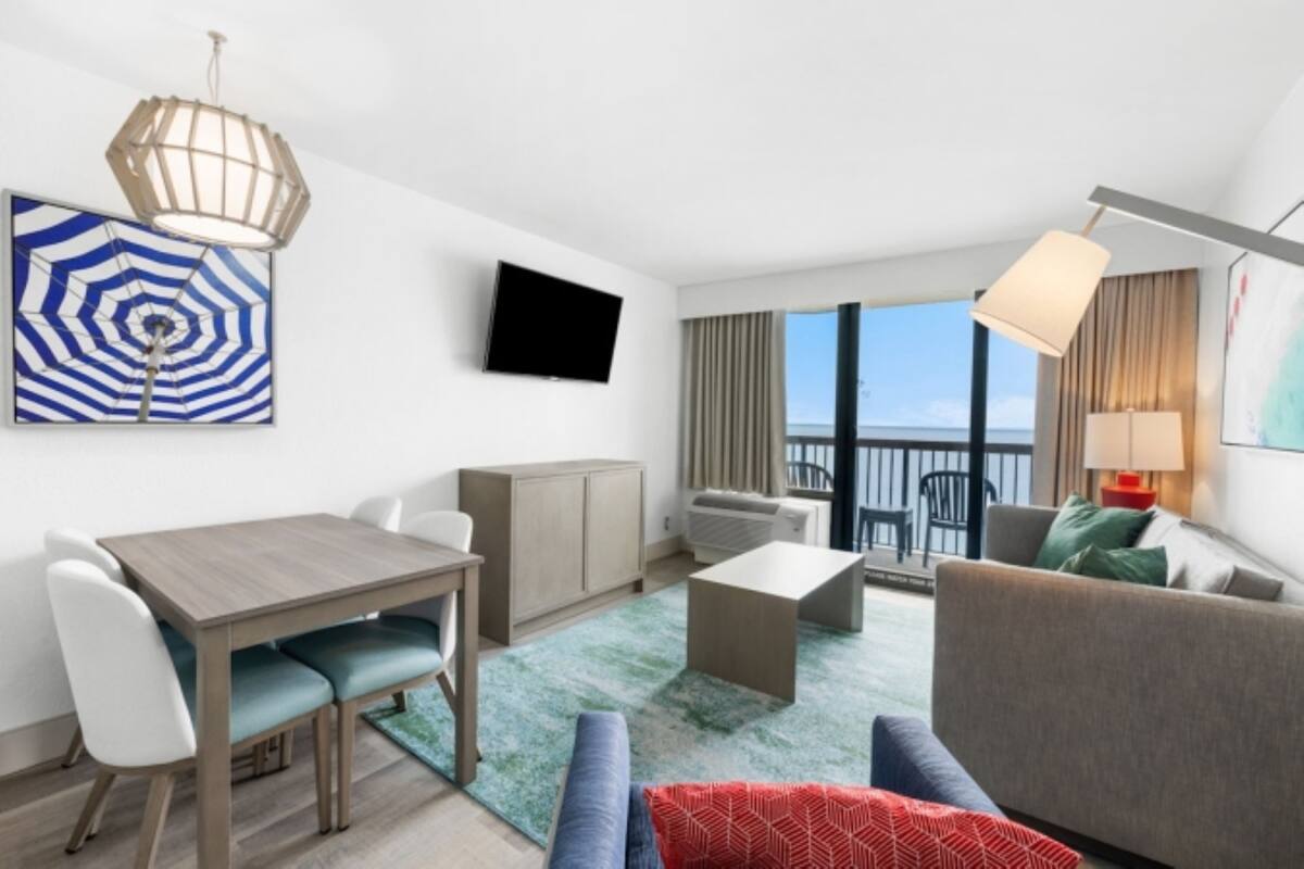 A modern hotel room with a dining area, a sofa, a coffee table, and a view of the ocean.