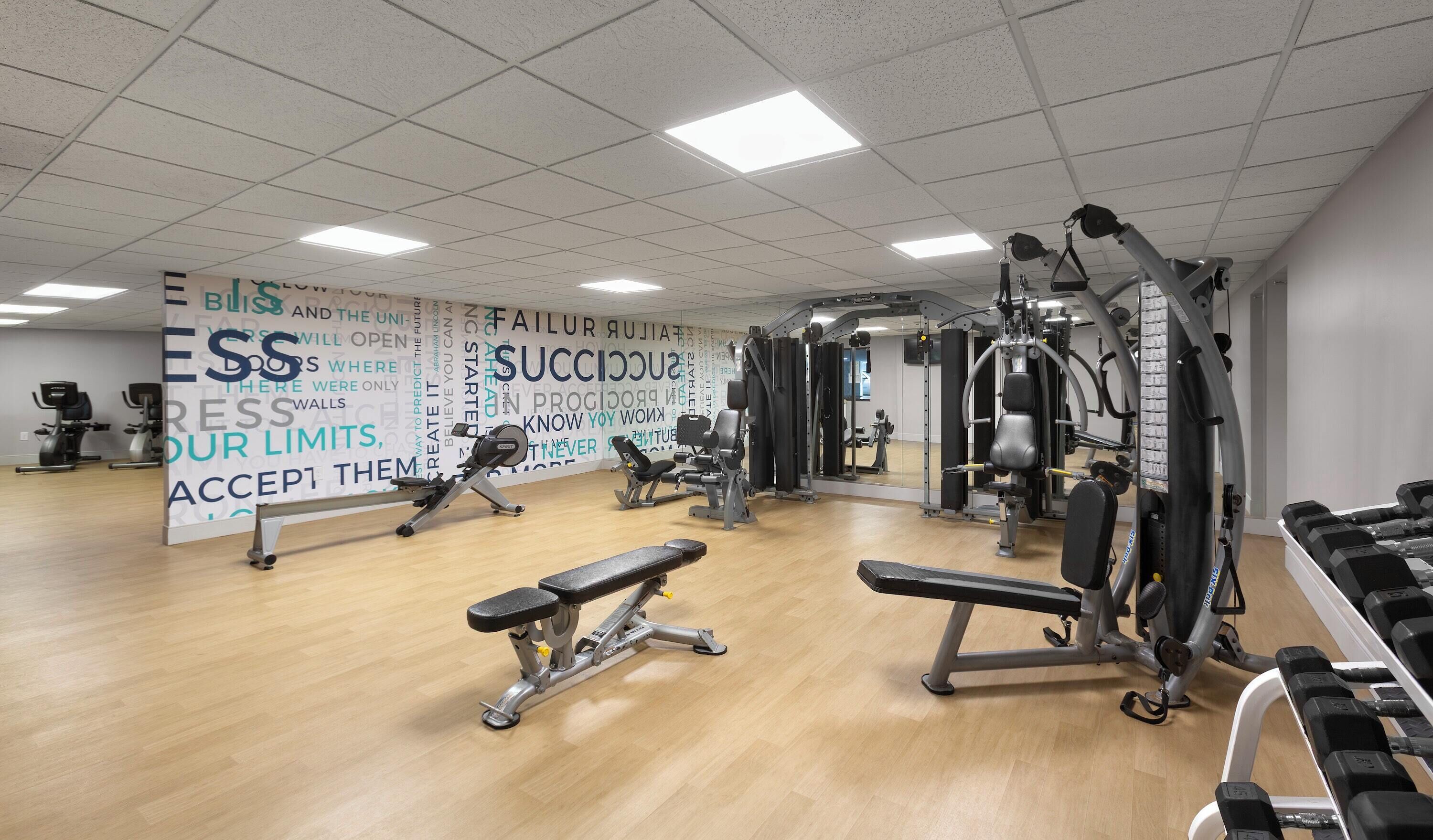 A gym with exercise equipment, a wooden floor, and motivational wall art.