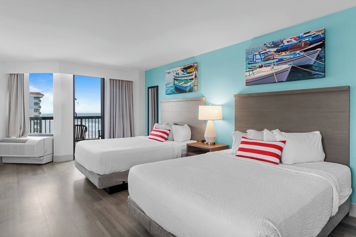 A hotel room with two beds, a balcony, a view of a building, and artwork on the walls.