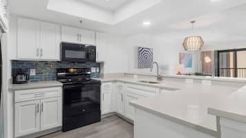 A modern kitchen with white cabinets, a black stove, a microwave, and a large island.
