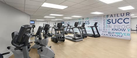 A gym with various cardio machines, a mirrored wall, and motivational posters.
