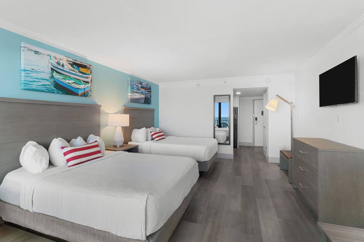 A hotel room with two beds, a TV, a desk, and artwork on the walls.