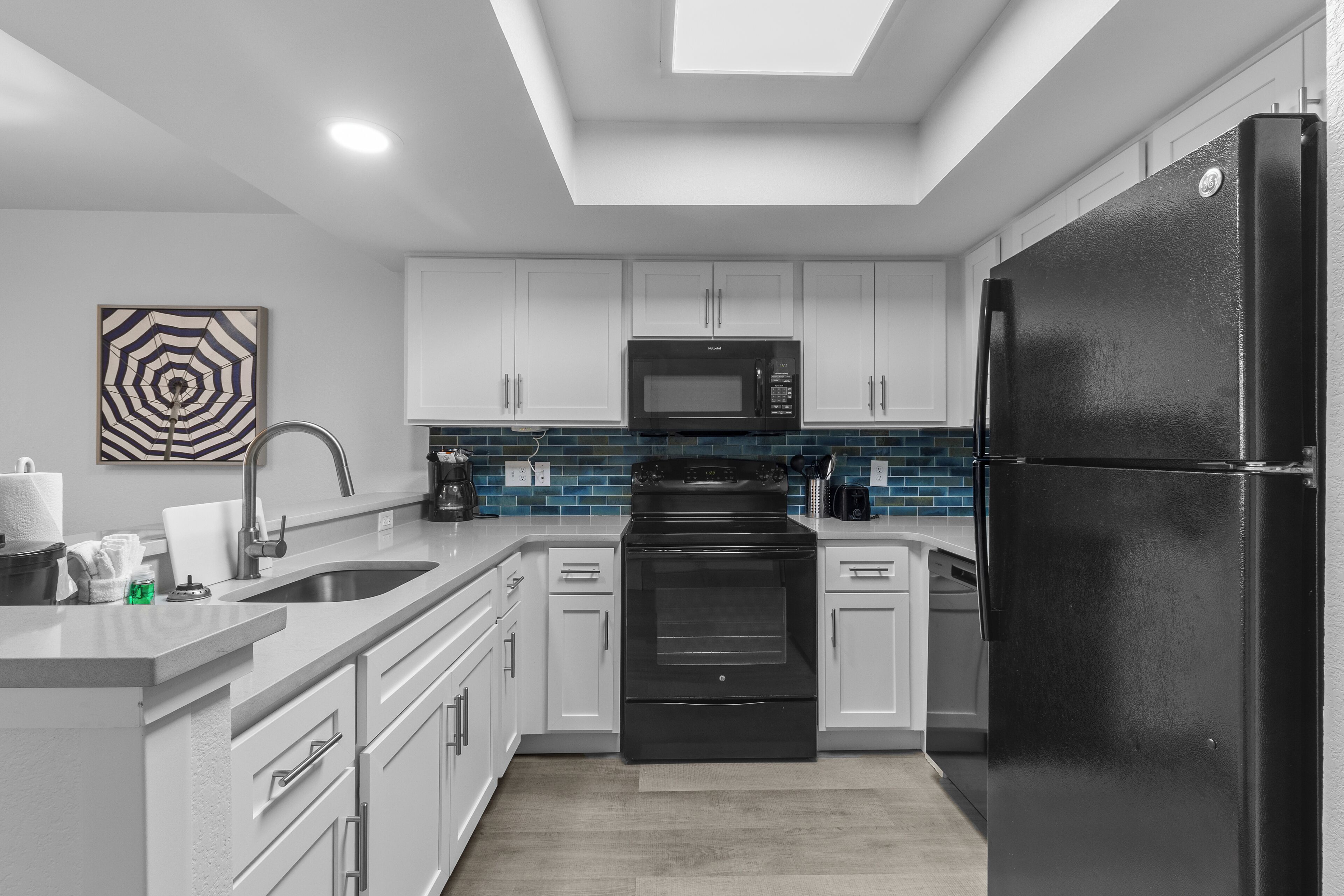 A modern kitchen with white cabinets, a black refrigerator, a microwave, and a stove.