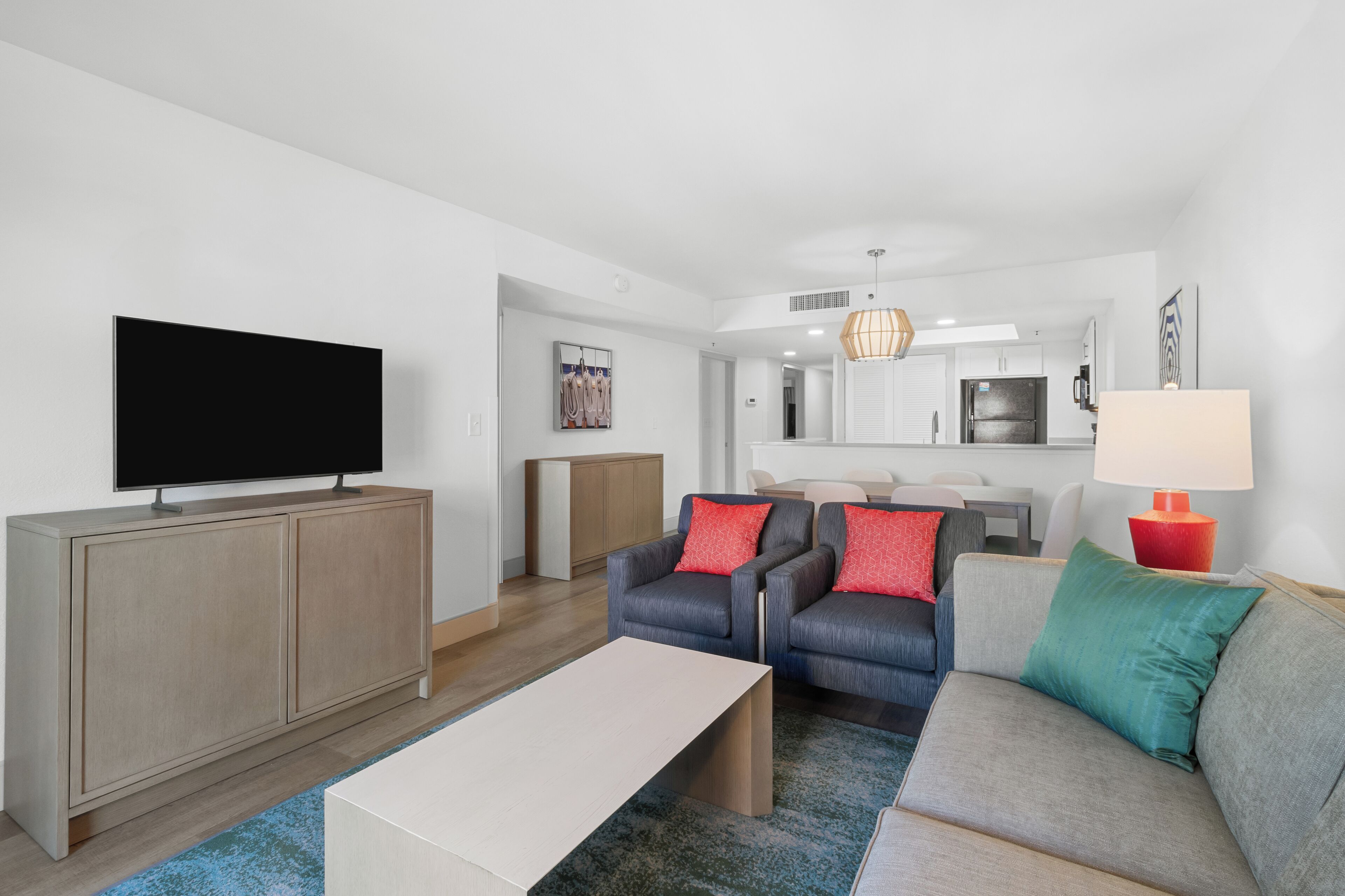 A modern living room with a flat-screen TV, two sofas, a coffee table, and a dining area in the background.