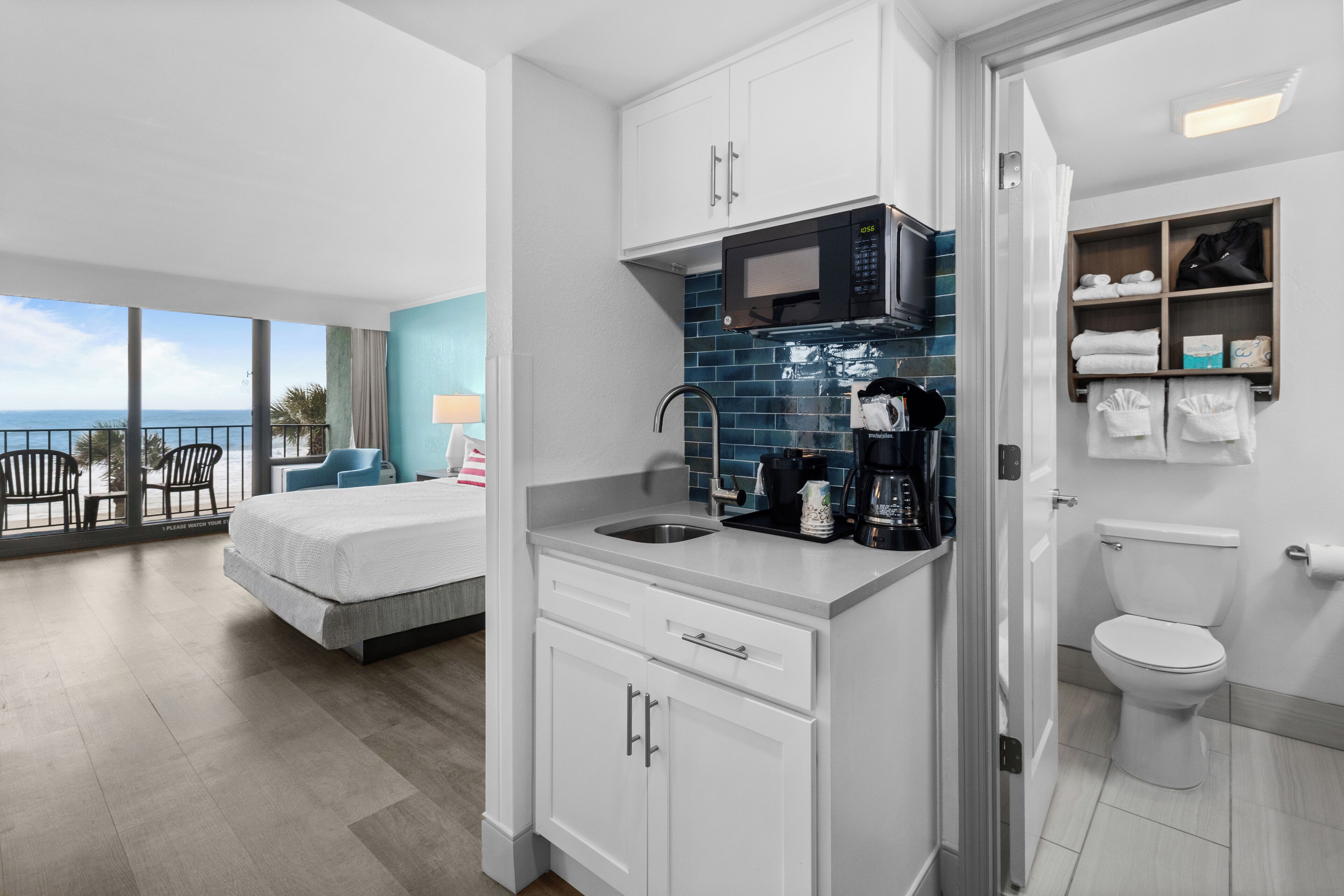 A modern hotel room with a balcony, a kitchenette, a bed, and a bathroom.