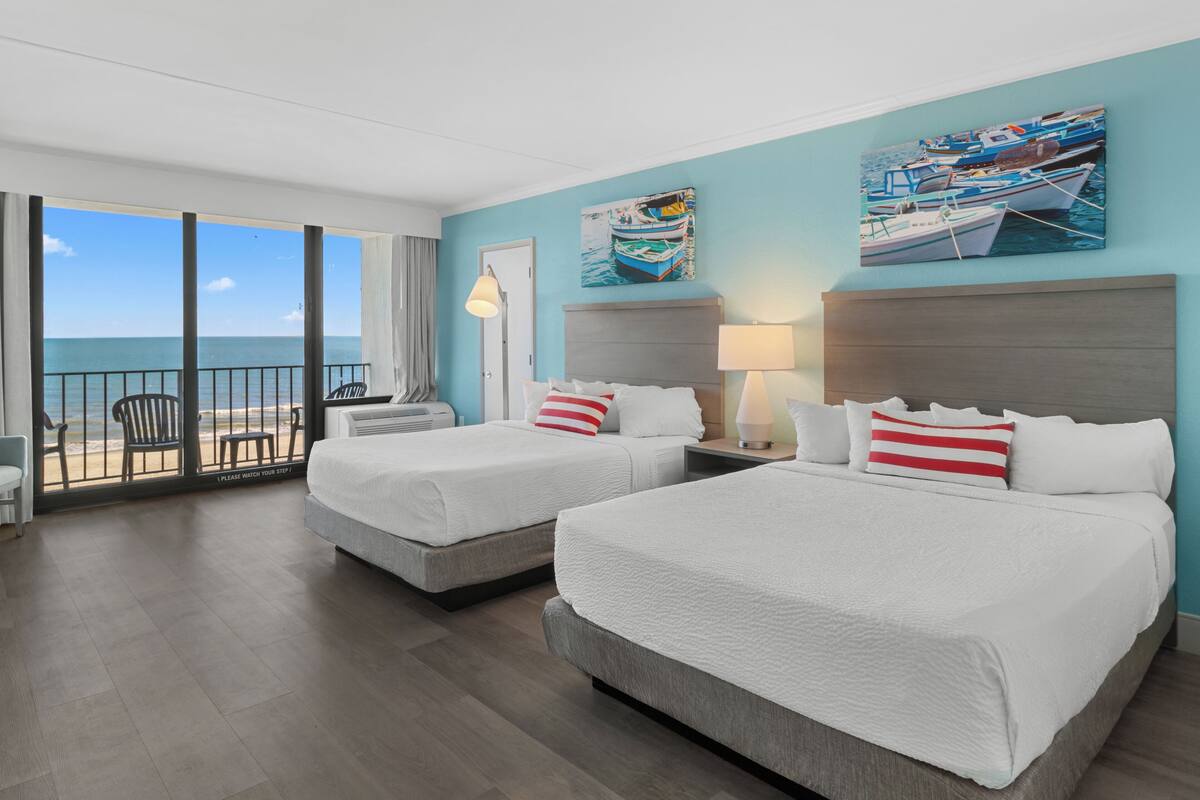 A hotel room with two beds, a balcony with a view of the sea, and artwork on the walls.